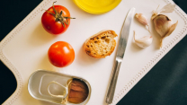 Tomatoes, bread, and sardines arranged for Catalán toast preparation.